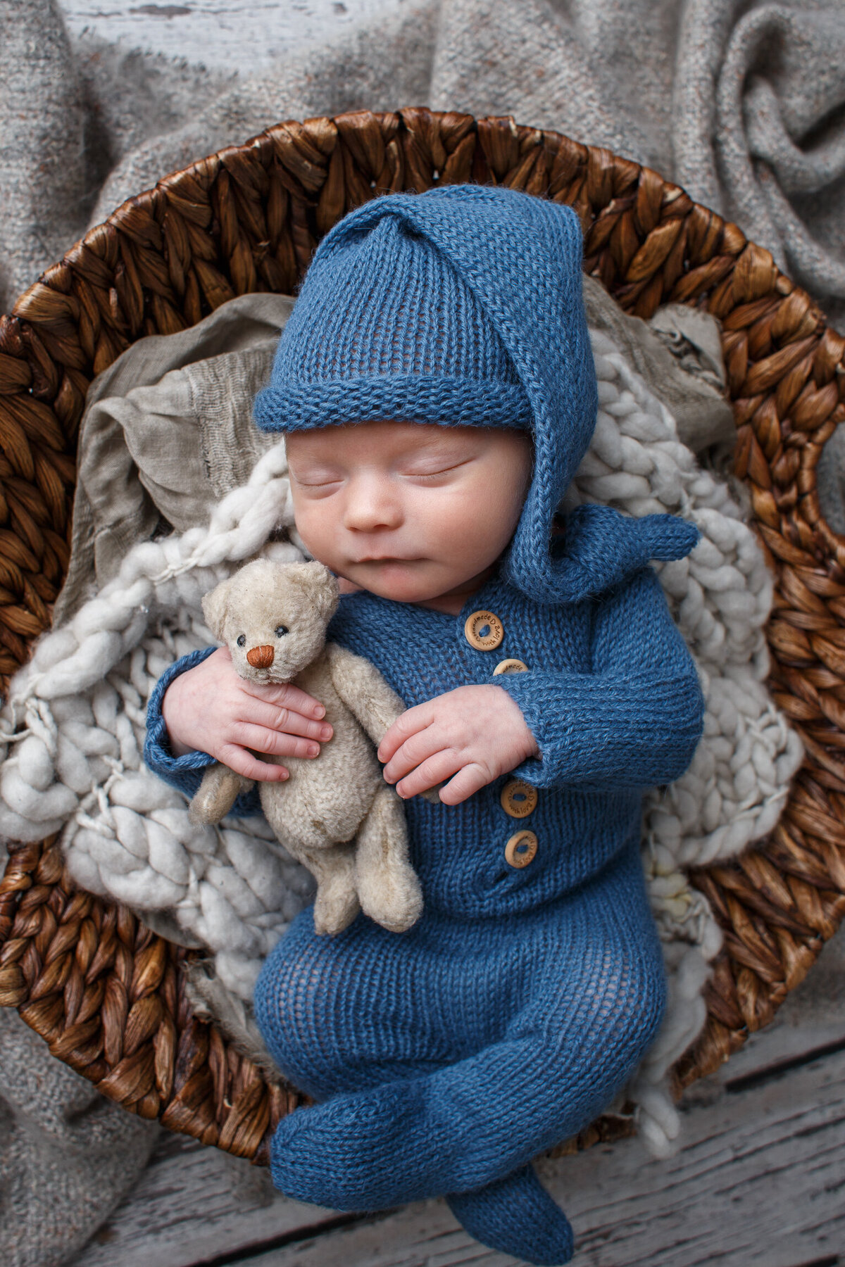 Newborn baby boy dressed in a blue sleeper and cap holding a tiny teddy bear