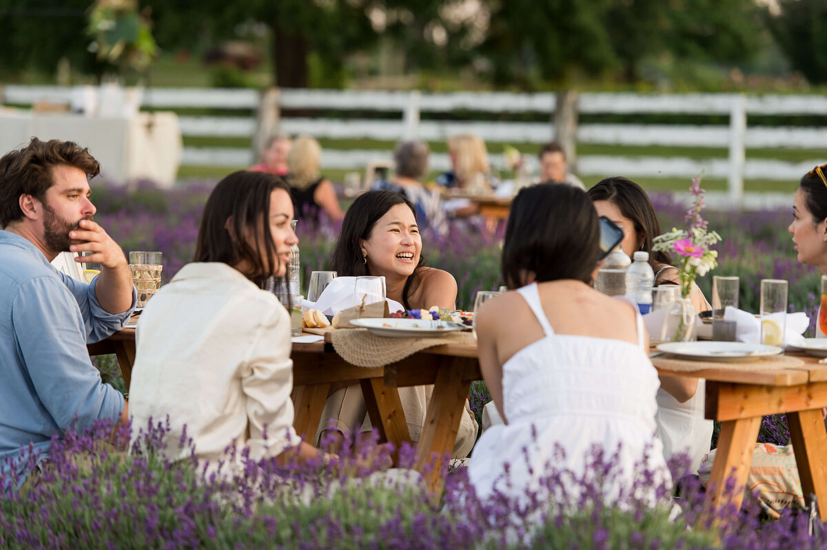 women dressed in white, laughing and sitting at a picnic charcuterie as part of Soiree in the Field.  Captured by Ottawa Event Photographer JEMMAN Photography COMMERCIAL