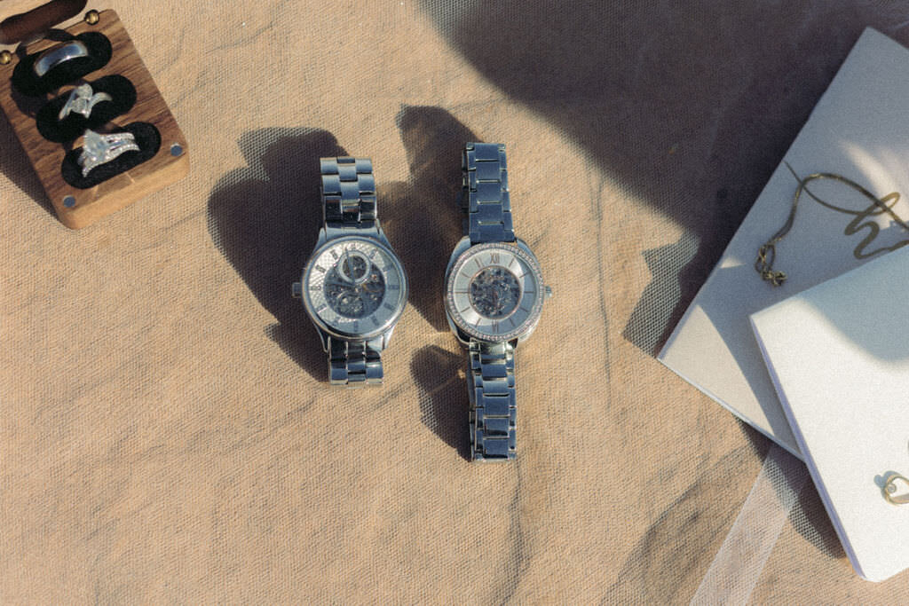 Two watches laid next to wedding rings and vow books.