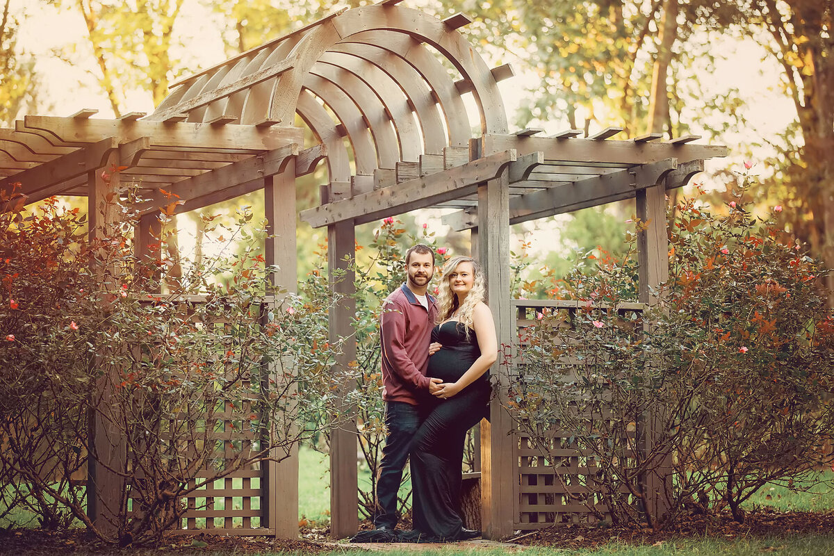expecting parents standing under a gazebo and holding hands