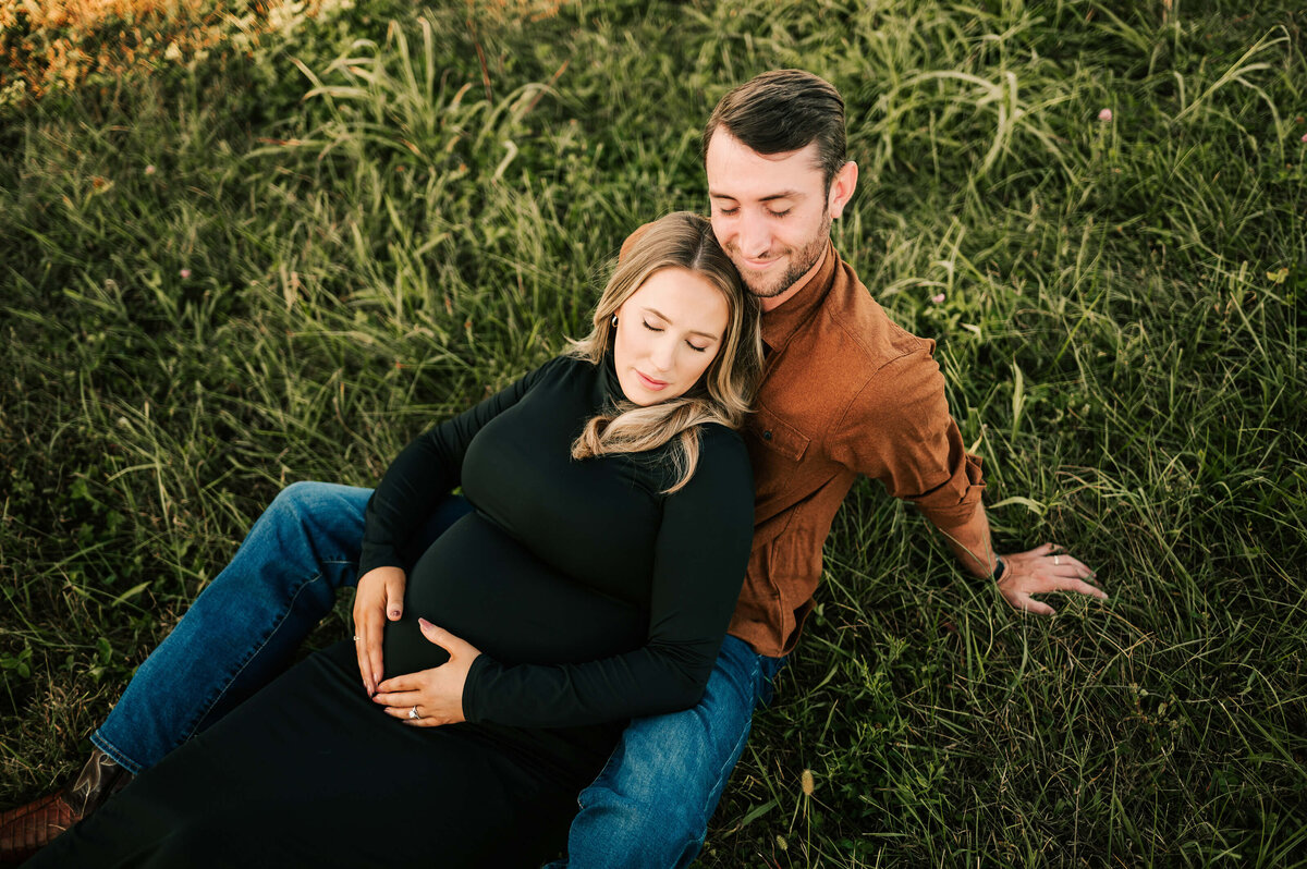 pregnant couple cuddling on green grass