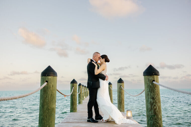 A breathtaking moment as the newlyweds embrace on a dock, surrounded by ocean views and a pastel evening sky. Destination wedding photography by Claudia Amalia Photography.