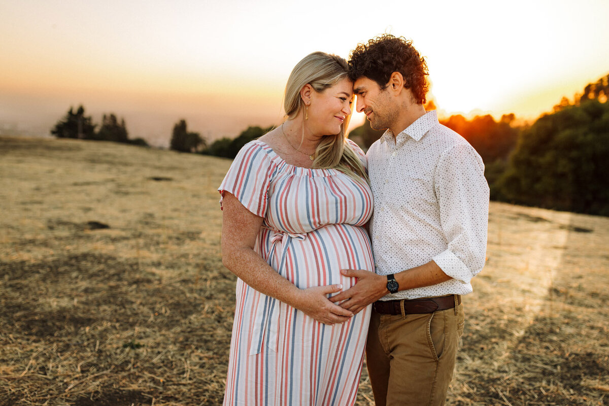 pregnant woman and her husband smiling at each other and standing close at golden hour at Bay Area park