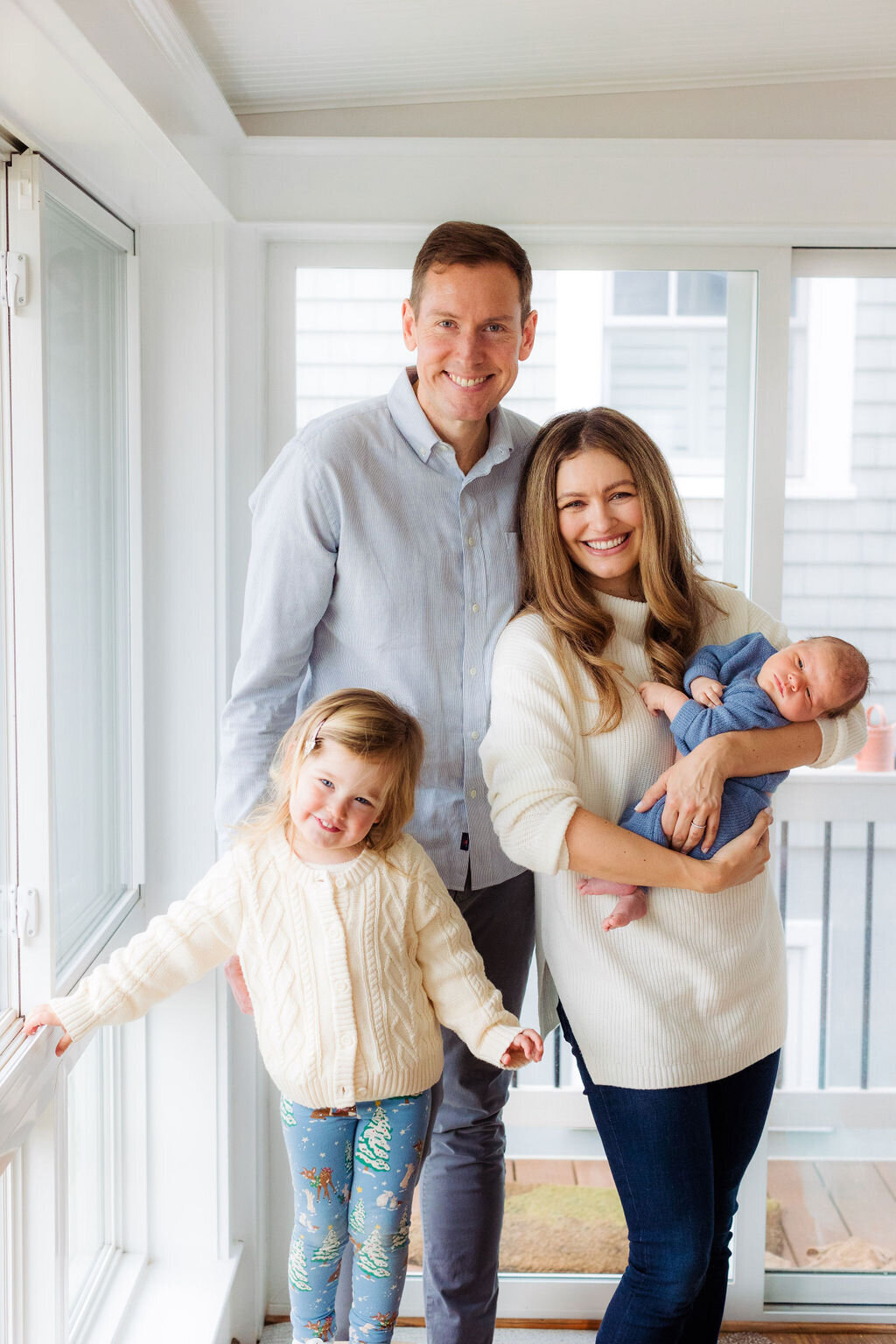 Two parents smile with their two children in a white room.
