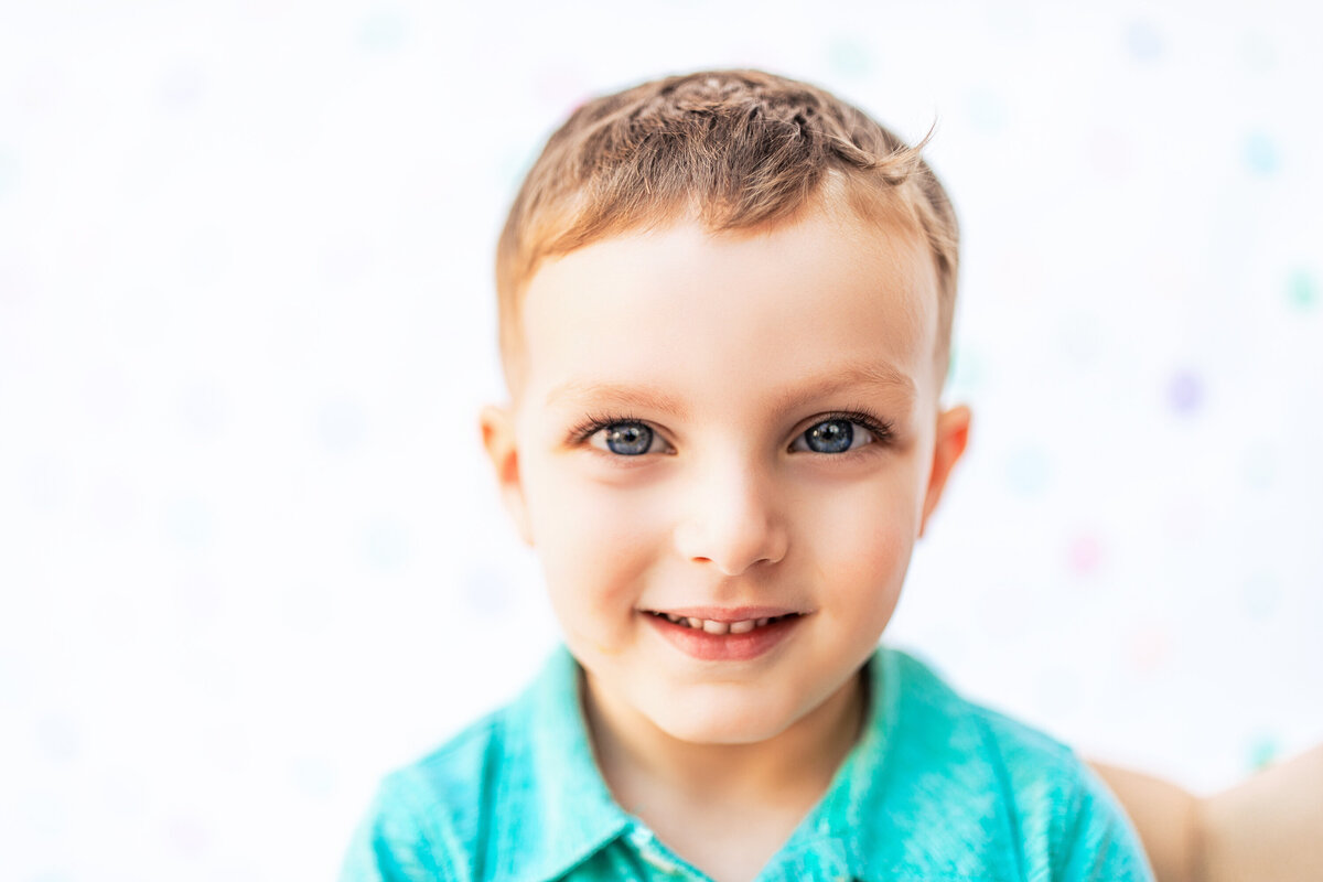 A blue eyed boy wearing a green top poses against a white background during an event near Pittsburgh Pennsylvania for a portrait