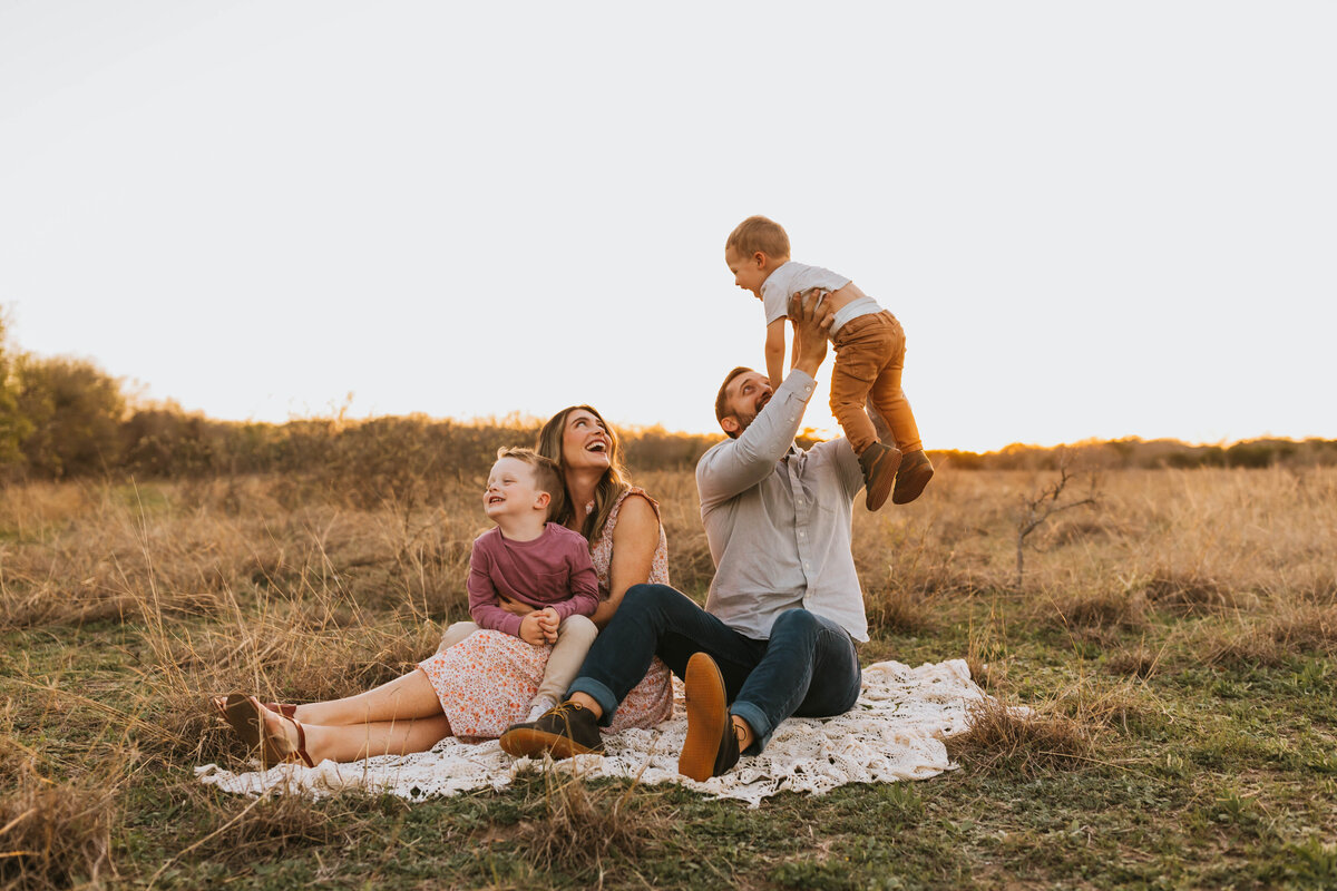 family of four sitting on a crochet blanket in a field at golden hour