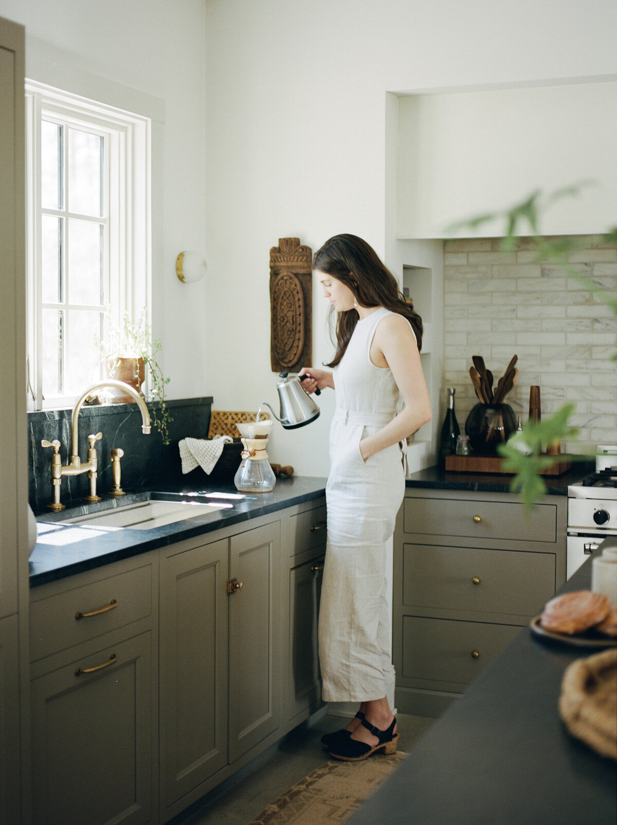 designer in a beige linen jumpsuit makes coffee at Fernhaus, Northern Michigan during her designer film brand photos
