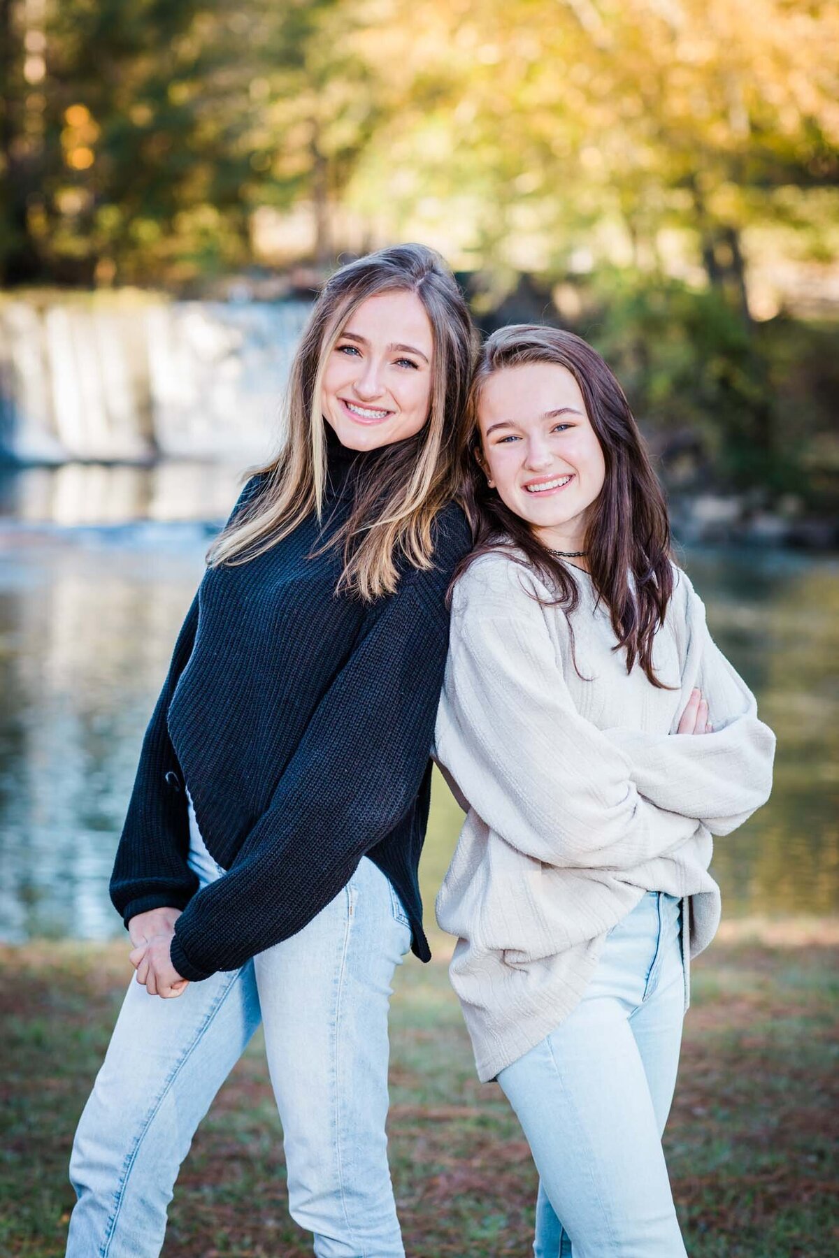 Two sisters lean against each other back to back and smilie at the camera for their portrait.