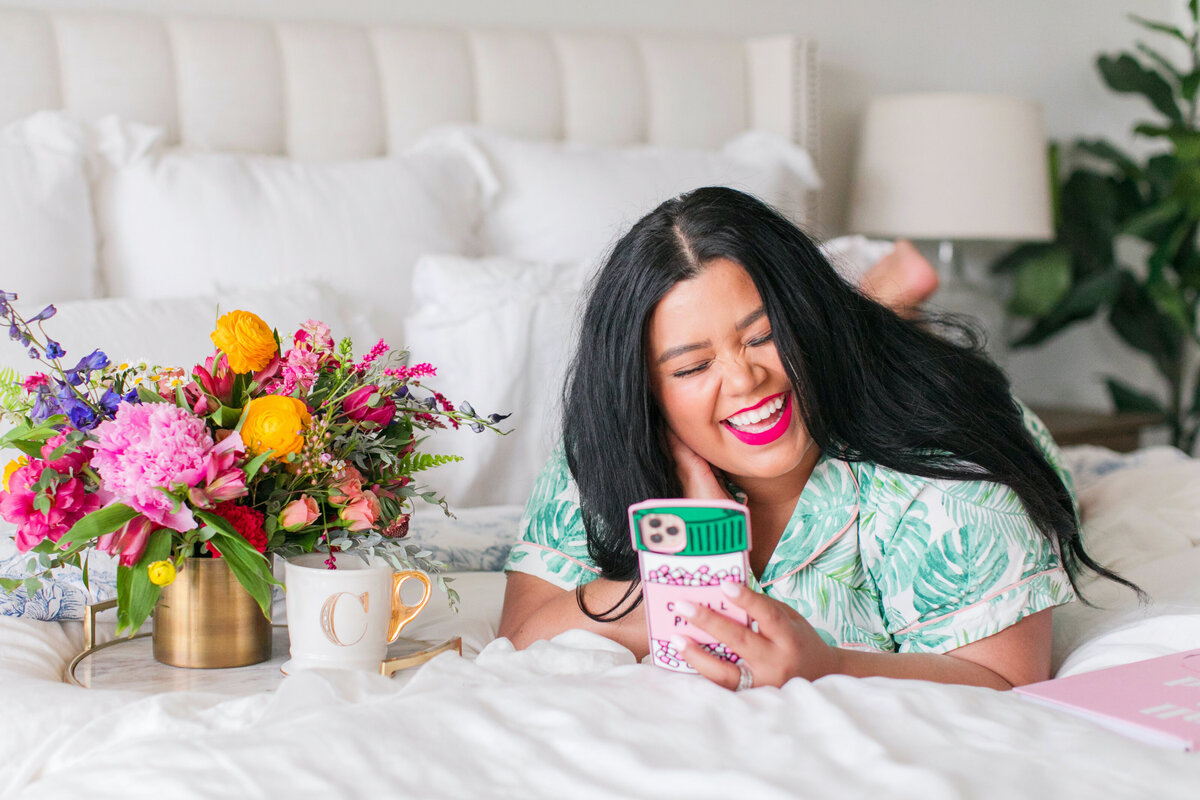 woman laying on bed laughing at phone