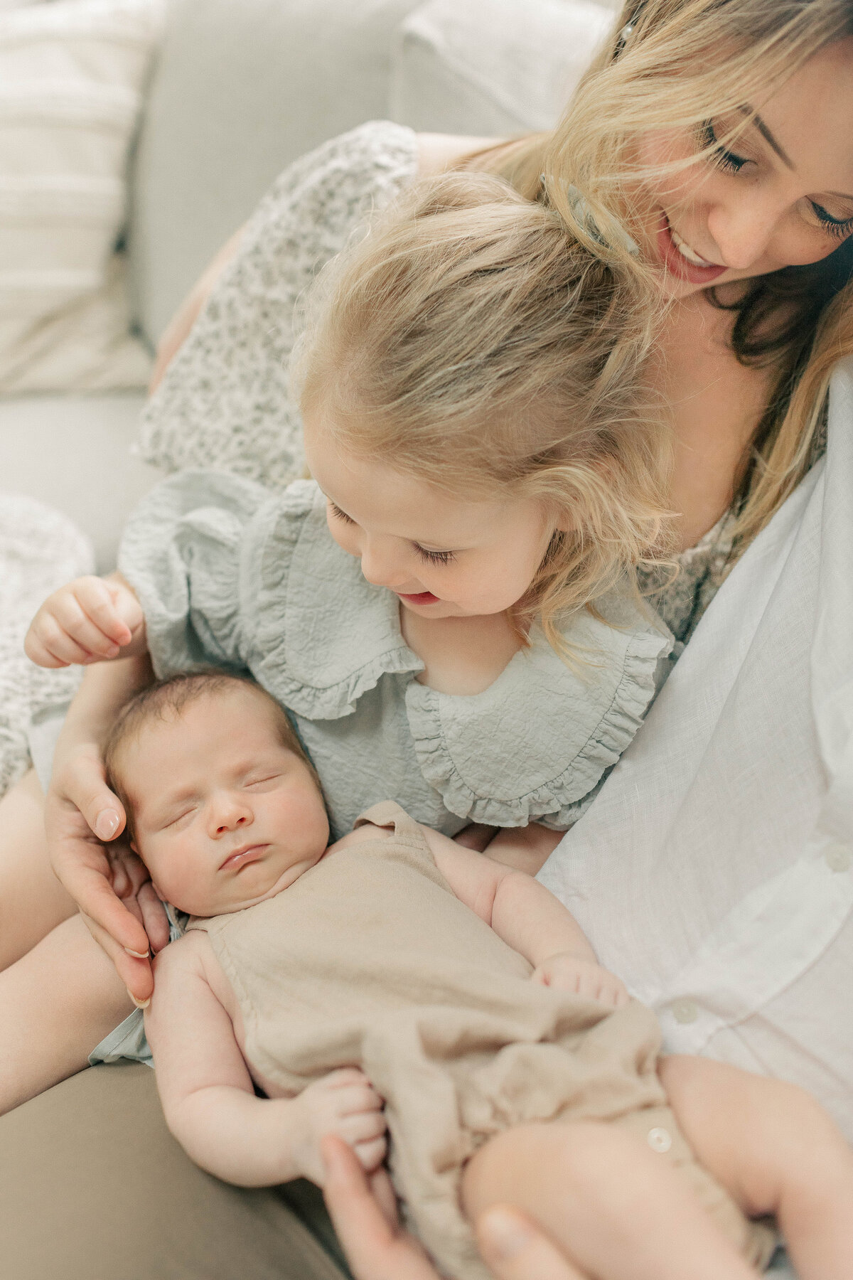 Mother sitting on a couch with her toddler daughter and newborn baby boy, all cuddled together during an in-home lifestyle newborn session in Kansas City.