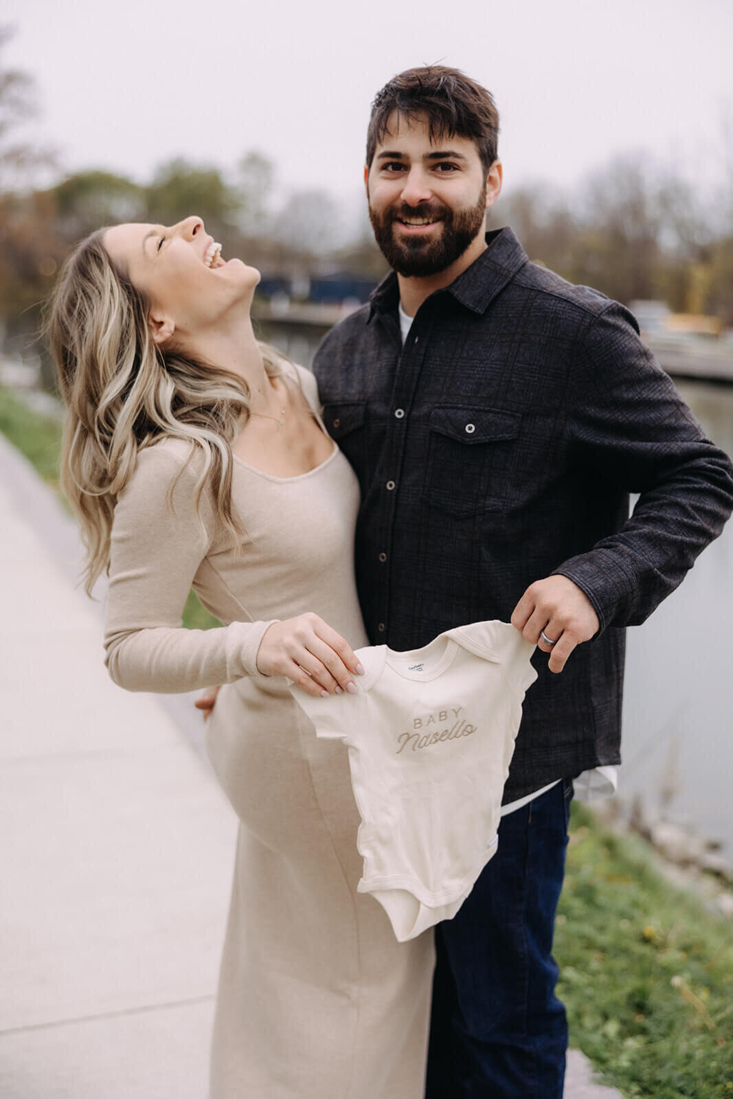 Man and woman holding baby onesie for baby announcement photos in Finger Lakes New York