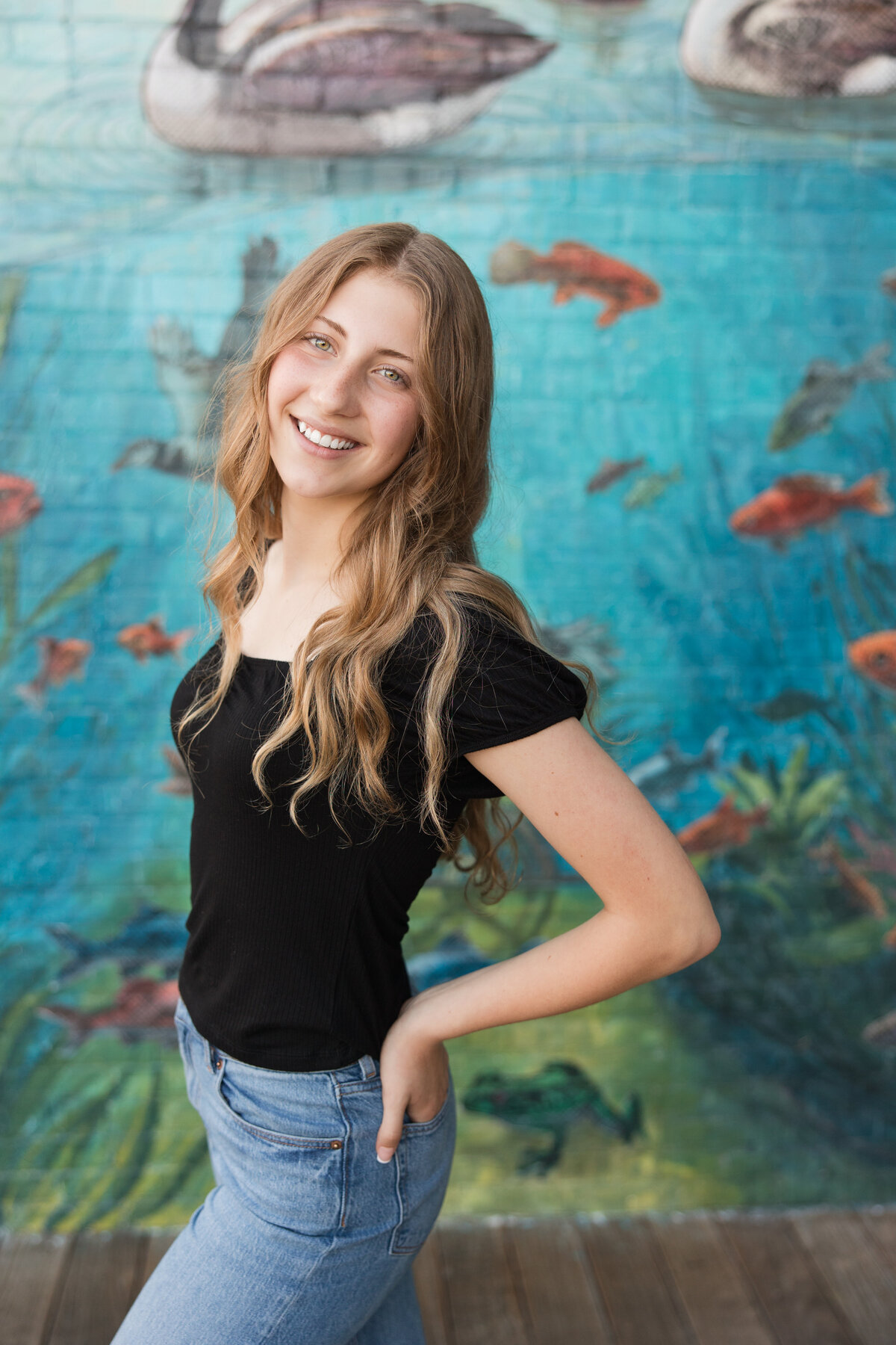 Senior girl standing in front of a mural smiling at the camera