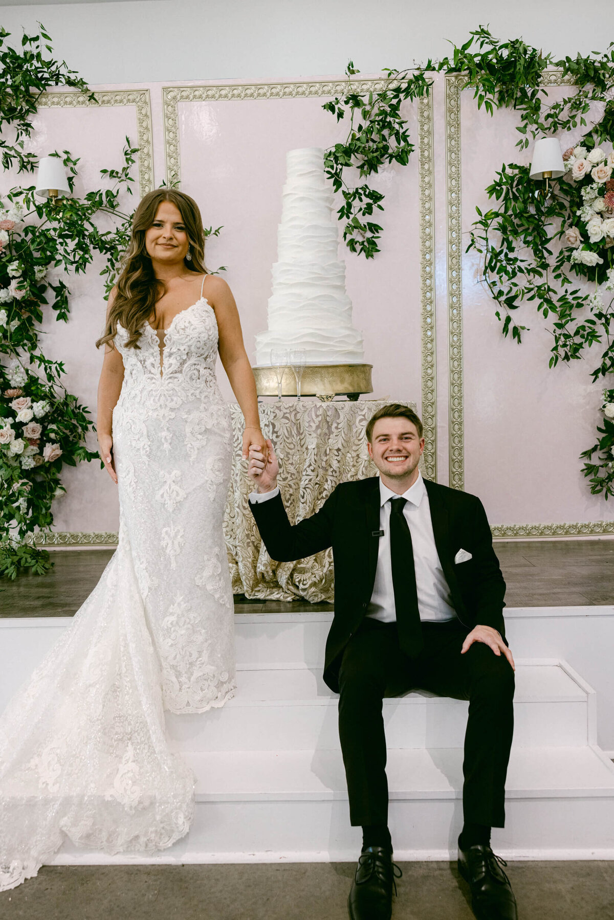 A wedding portrait of the bride and groom with their white wedding cake behind them