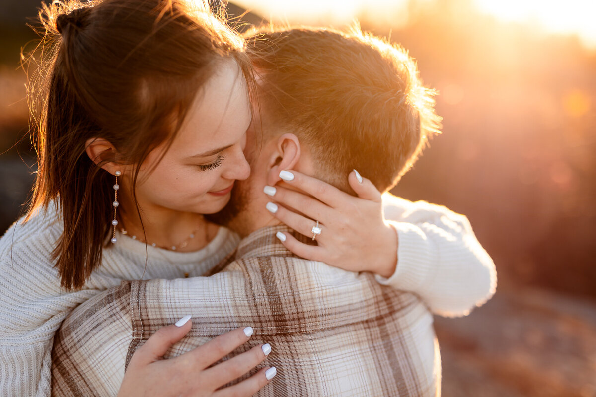 Engaged couple hugging as girl wraps her hands around guys neck to show off engagement ring.