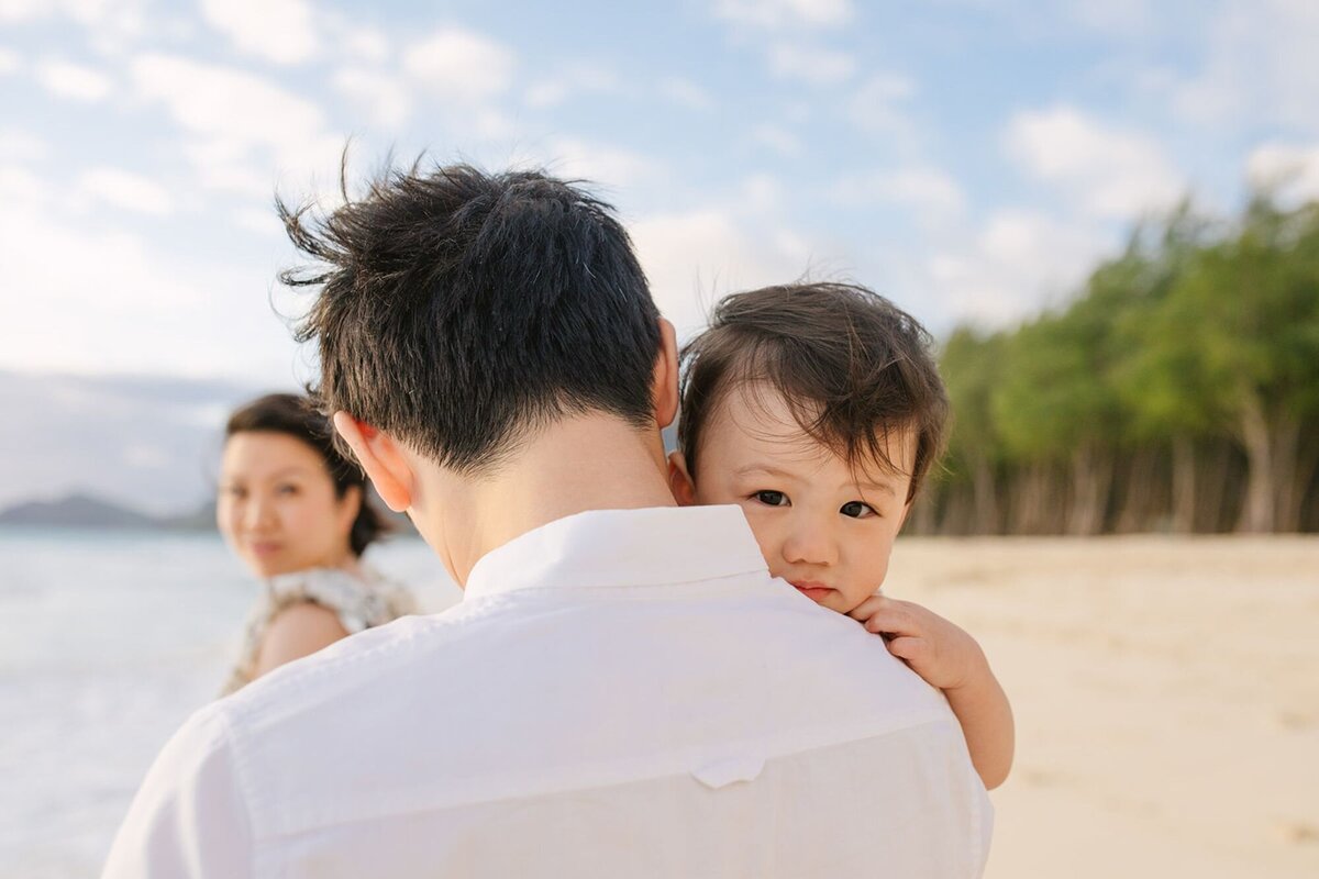 A man holds his baby as he walks with his wife along the beach.