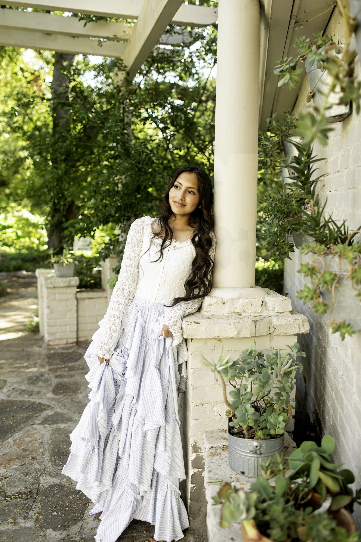 A senior walking along the winding garden paths at Chandor Gardens, Weatherford, TX, surrounded by blooming flowers and peaceful scenery in her graduation photoshoot