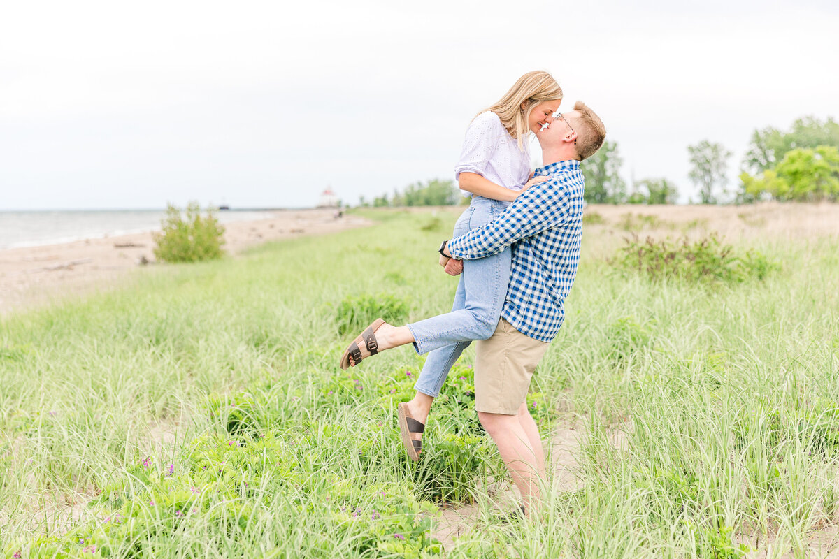 Light and airy beach engagement session lift and kiss with foot pop in the beach grass at Mentor Headlands Beach