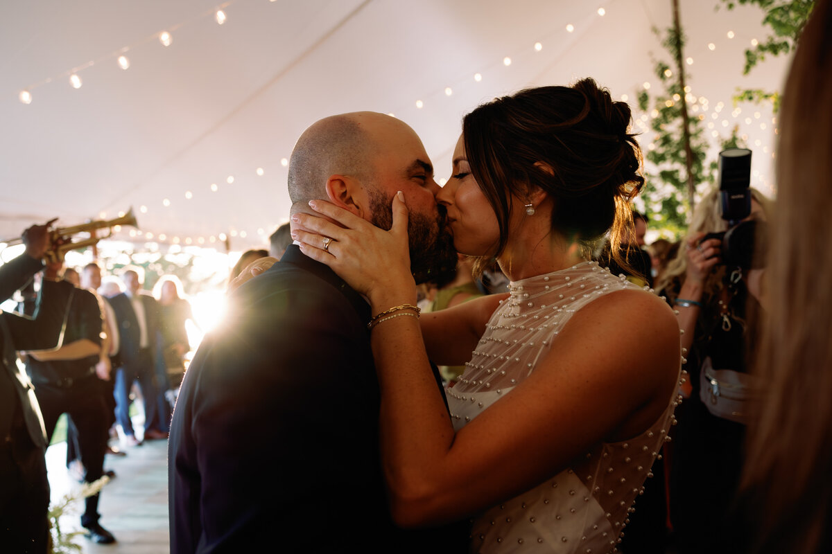 Bride and groom kissing at their fall tent wedding reception in rhode island warm lighting 