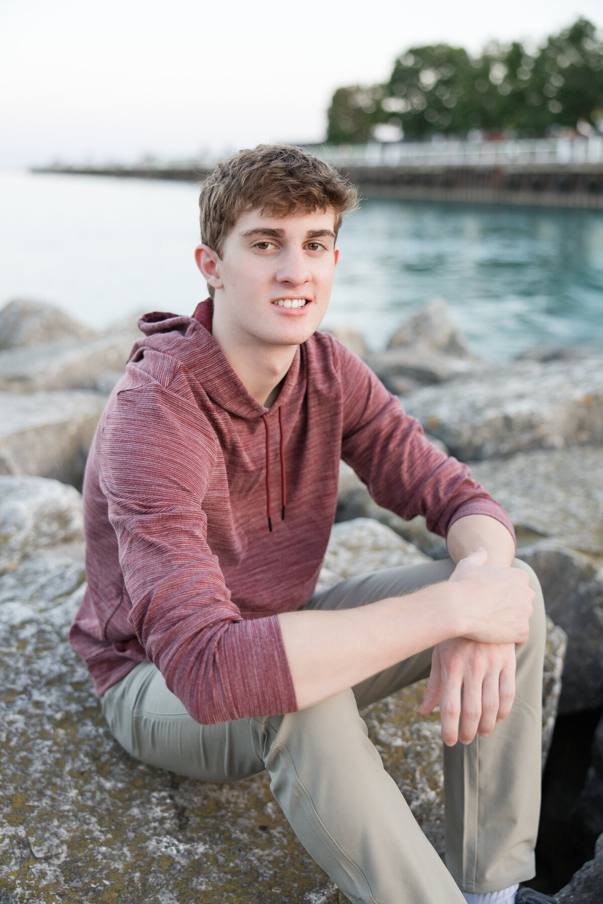 Senior guy sitting on some rocks by Lake Michigan, looking at the camera