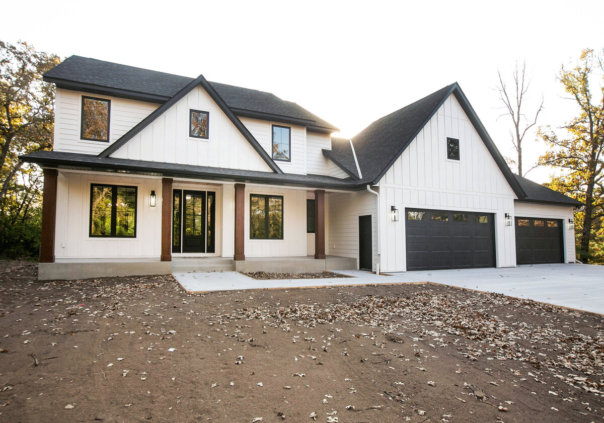 Exterior view of custom home in Big Lake Township, Minnesota with farmhouse details, cream siding, wood pillars and front porch built by Cornerstone Custom Builds