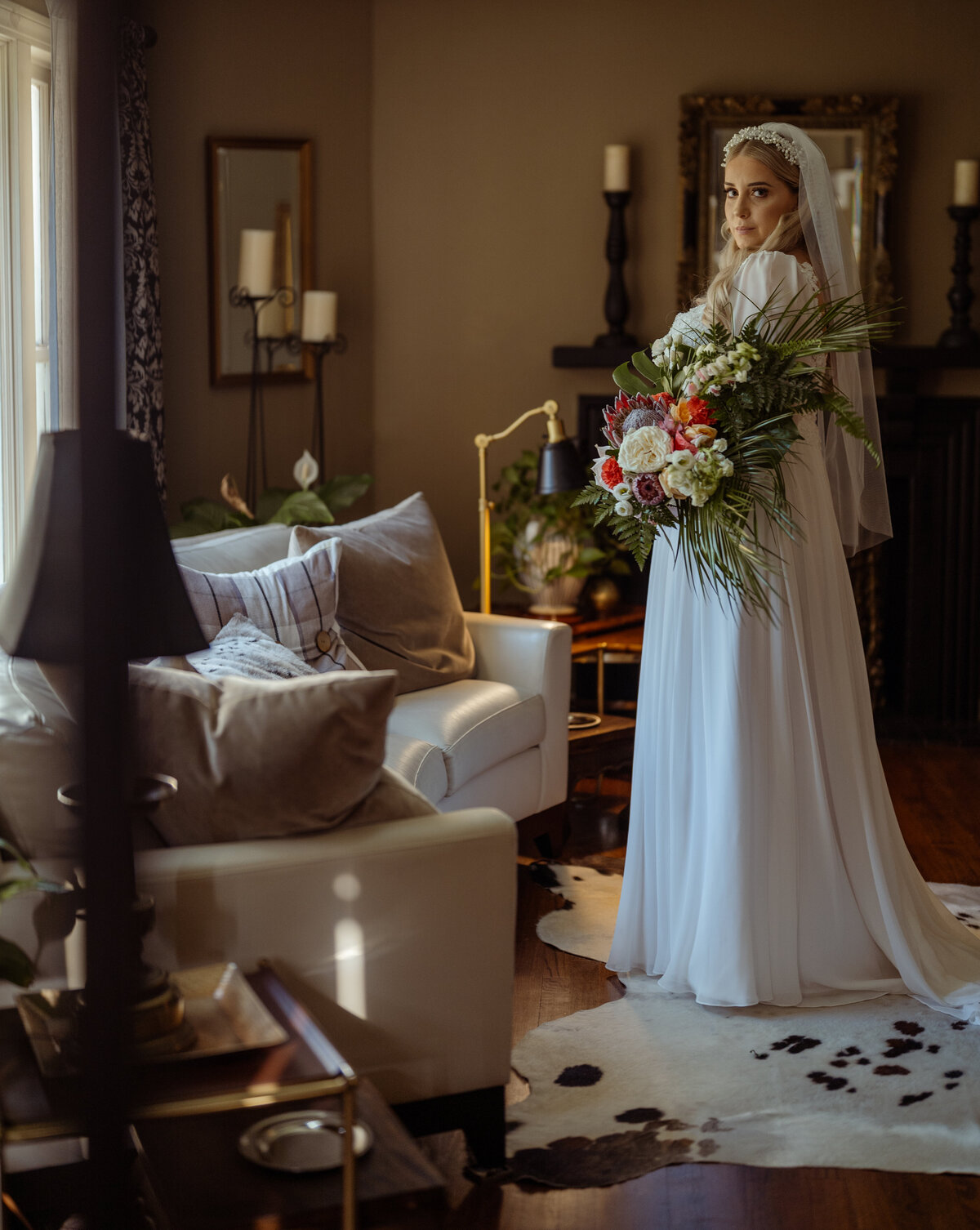Elegant bride standing moments before her ceremony in a beautifully decorated room, dressed in a vintage-style gown with a flowing veil. She holds a lush tropical bouquet, creating a stunning contrast in this intimate pre-ceremony portrait captured in the Fort Worth area.