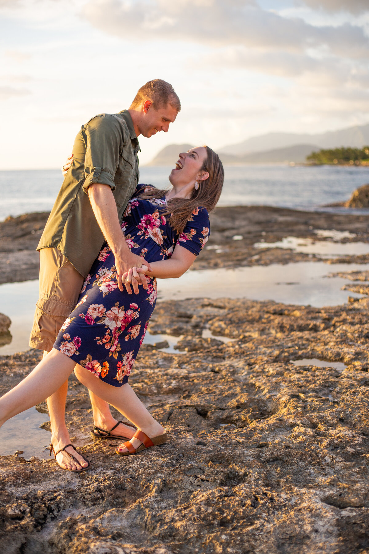 a smiling man dances with his wife on the beach as she laughs