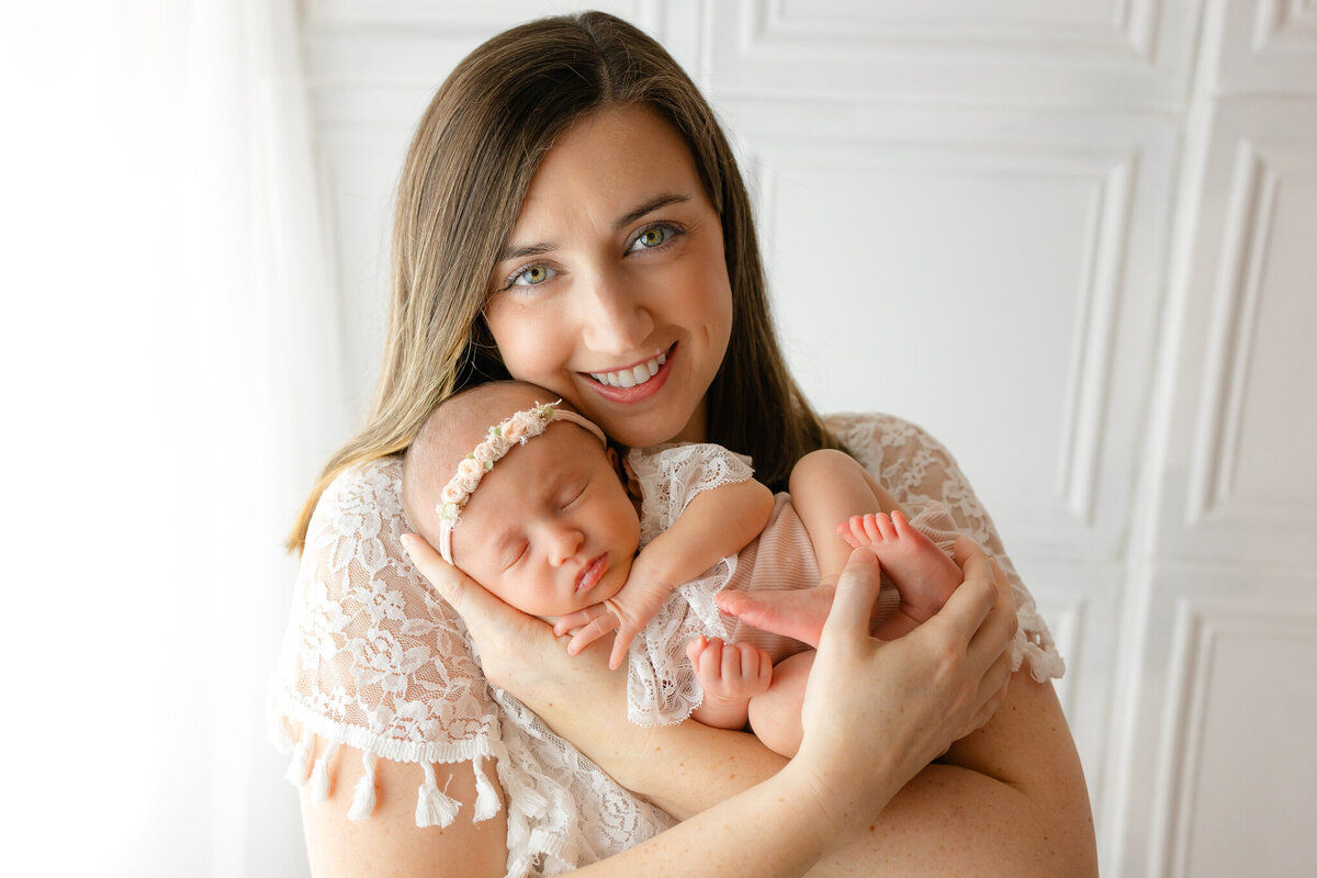 Young mom holding her baby girl wearing an heirloom outfit with her mom holding her