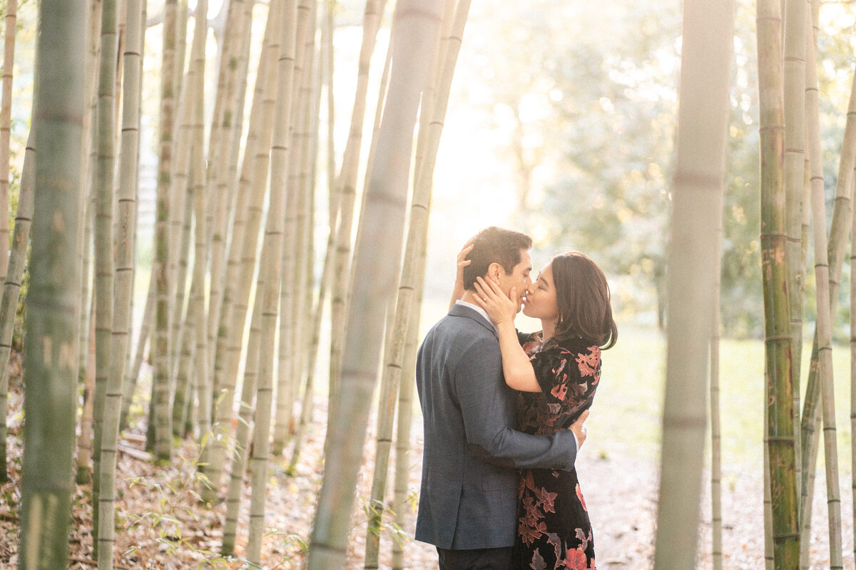 Couple kissing amidst tall bamboo stalks, with soft sunlight filtering through the leaves