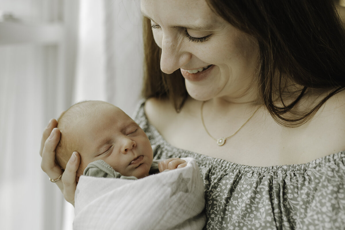 Verona B Photography captures an adorable sleeping newborn baby held lovingly by his mom as she tenderly gazes at him and smiles. It is such an honor to capture these moments between a new baby and his momma in an in-home newborn session near Akron, Ohio.