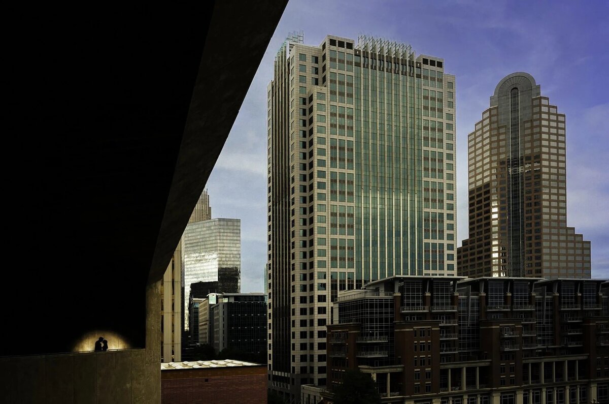 A view of city skyscrapers from a darkened architectural overpass, showcasing the contrast between shadow and urban structures.