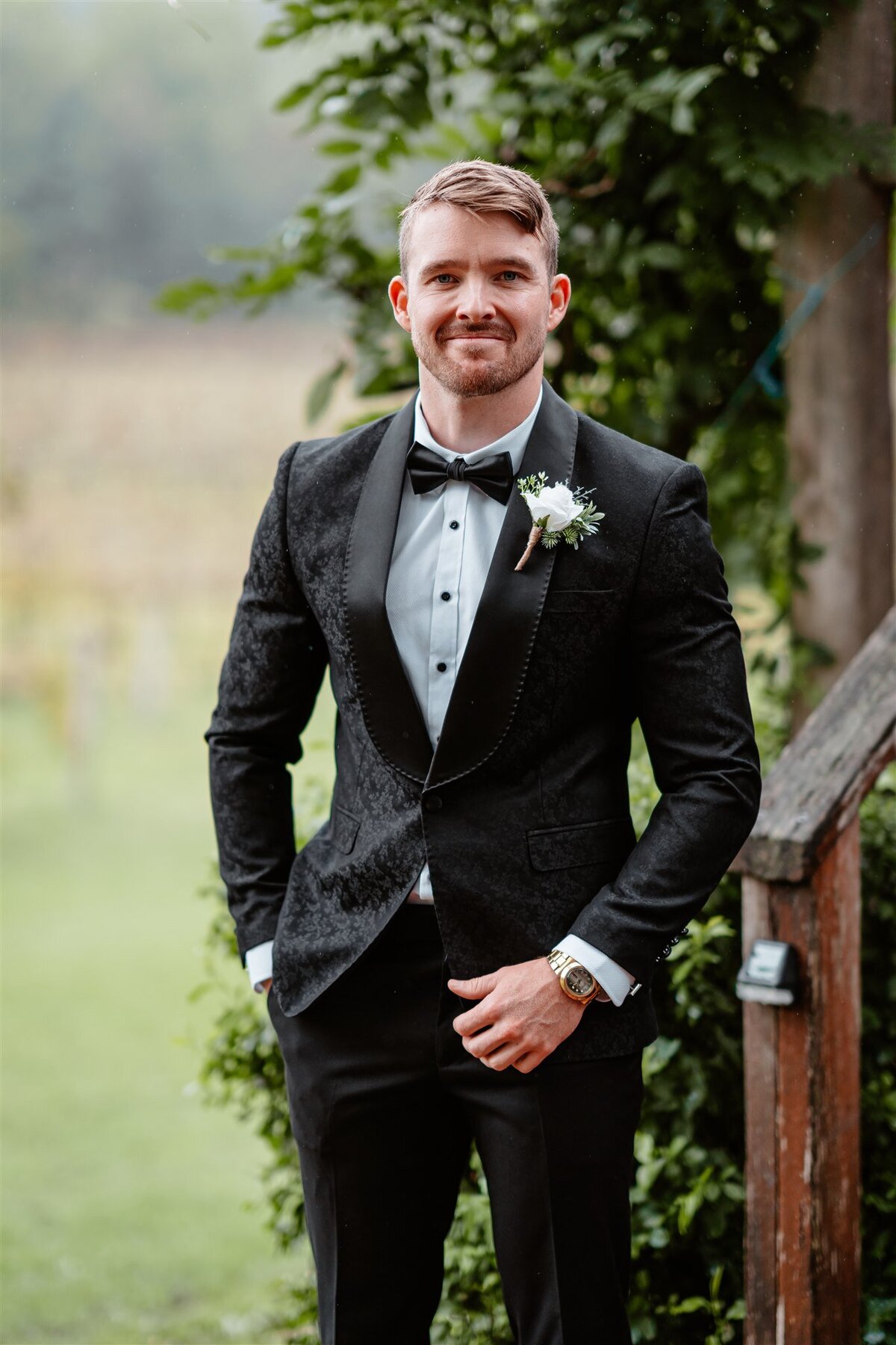 A groom poses for a photoshoot, exuding timeless elegance in a tailored suit against a scenic backdrop.