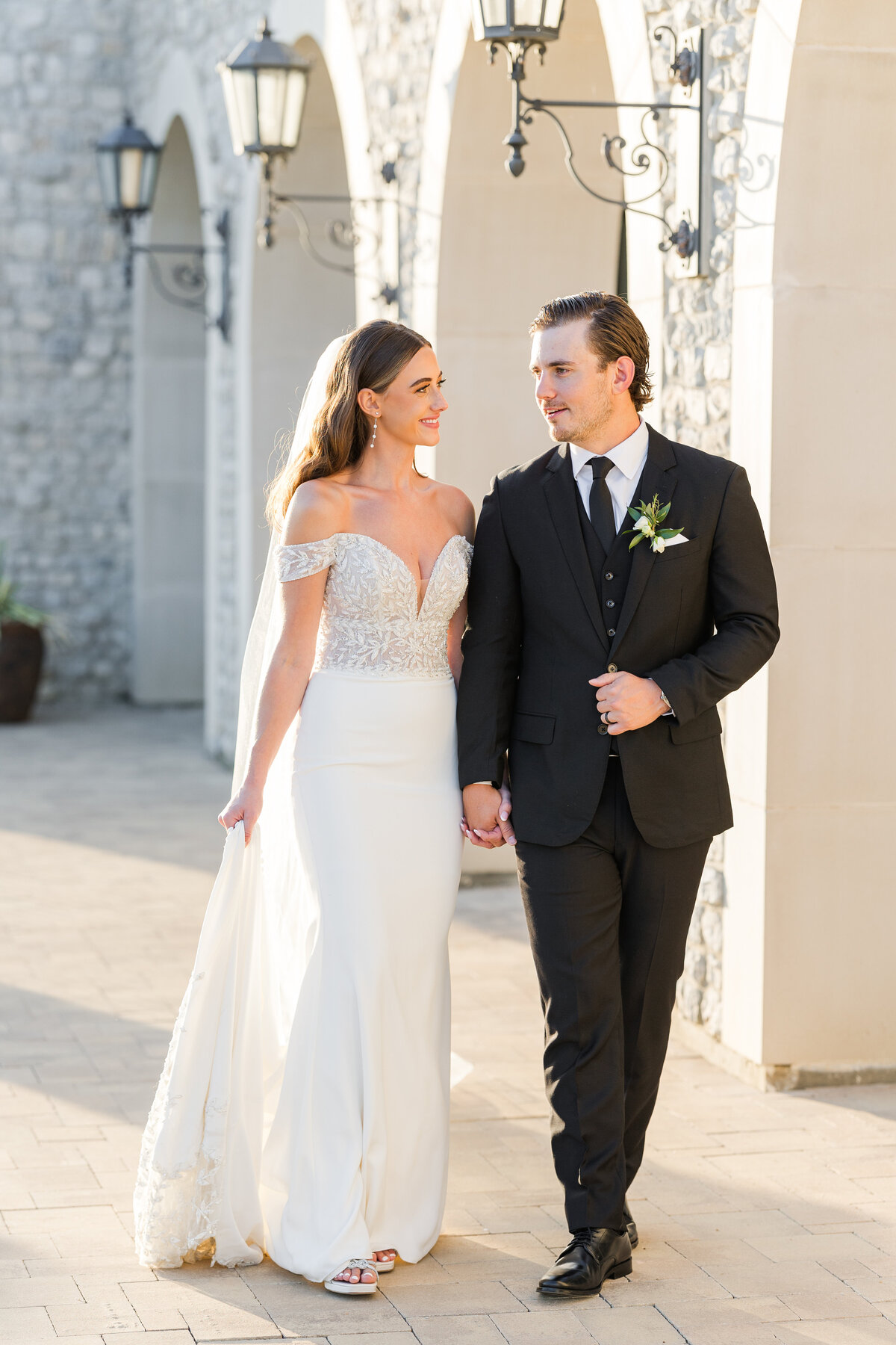 A sophisticated bride and groom walk hand in hand outside a European-inspired venue in Westlake, Texas. Captured during golden hour, this image highlights timeless wedding photography in the greater DFW area.