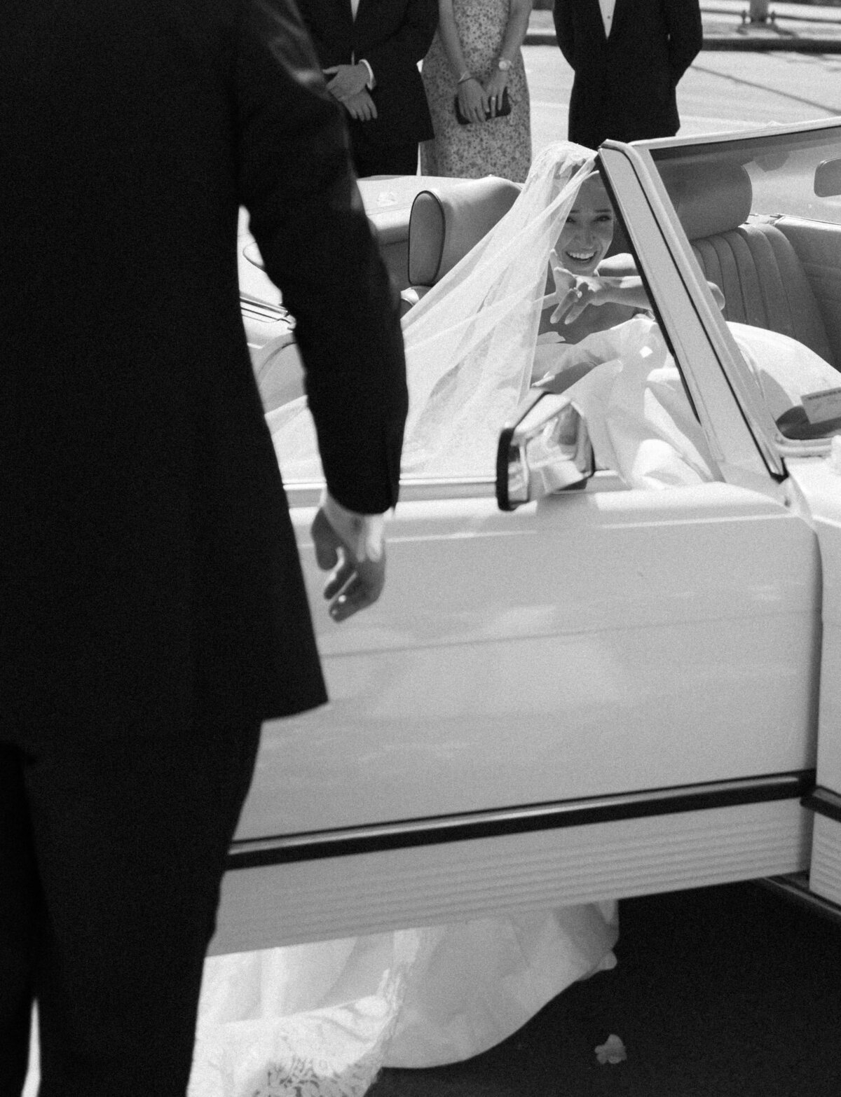 A groom closes the door of a vintage mercedes convertible for his bride in Detroit, Michigan