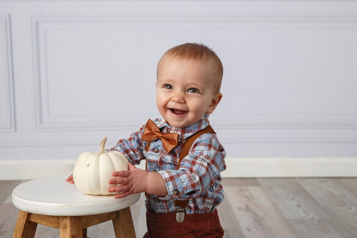 Portrait of a cute one year old kneeling with a pumpkin on a stool