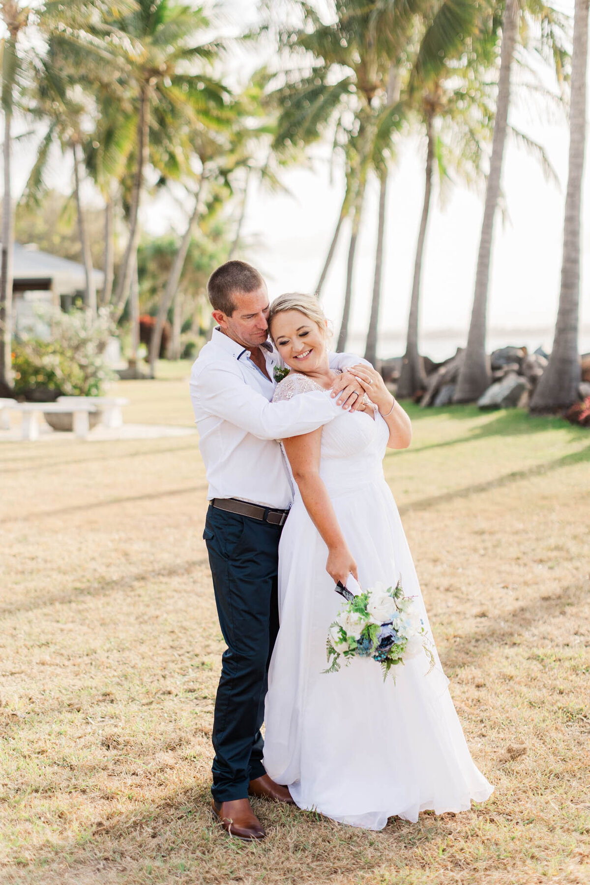 groom hugs bride under palm trees on their mackay wedding day