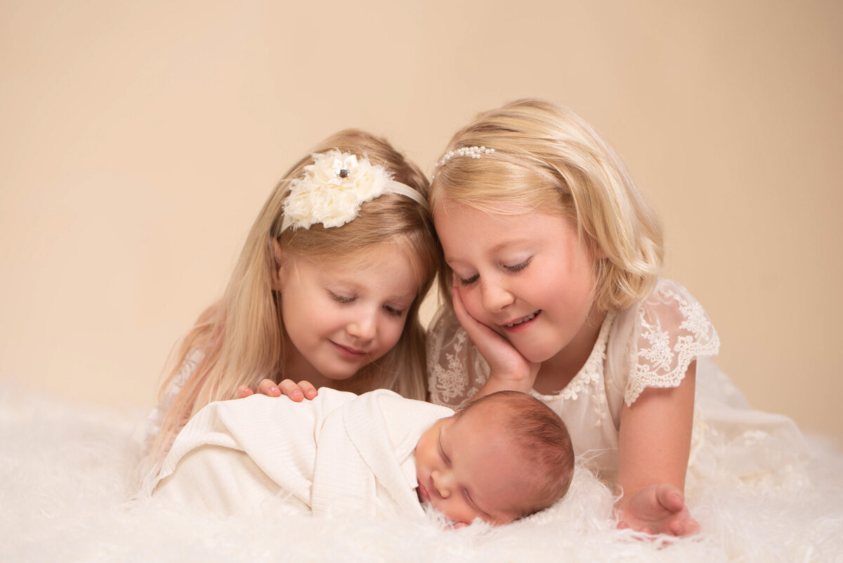 Adorable siblings cuddling their newborn baby sibling on a cozy blanket, captured in Overland Park, Kansas. Perfect for families looking to include siblings in their newborn photography session.