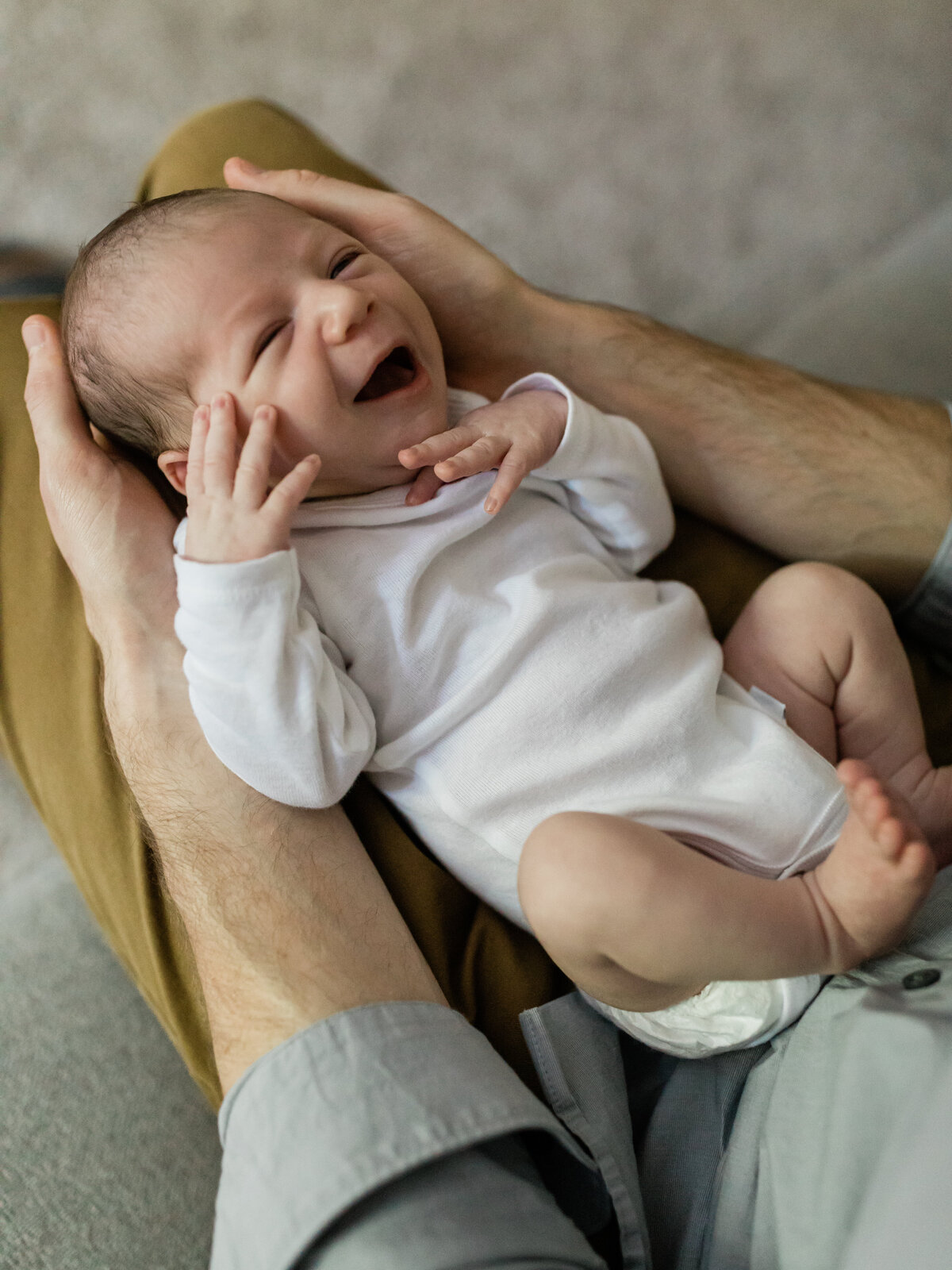 newborn baby boy laying in dads lap for in home lifestyle session