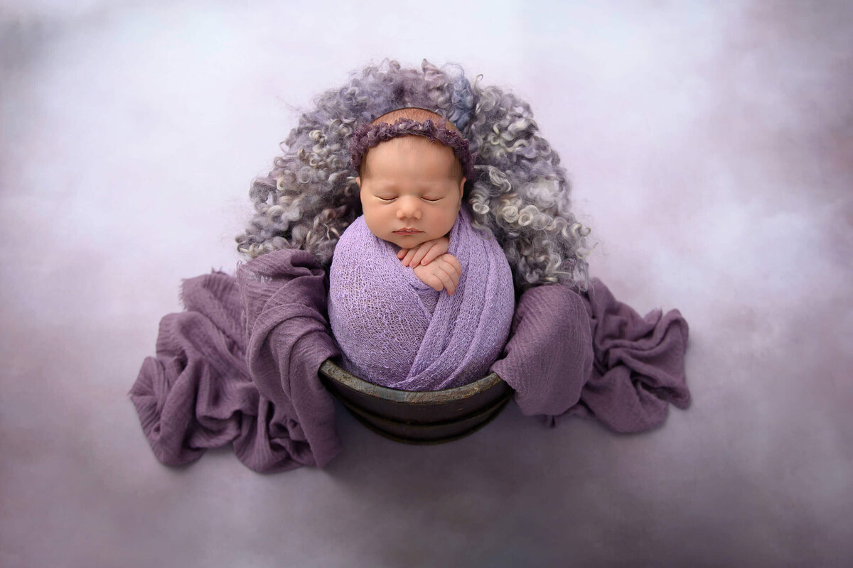 Baby girl wrapped in purple on a purple background for her Burlington, Ontario newborn photography session.