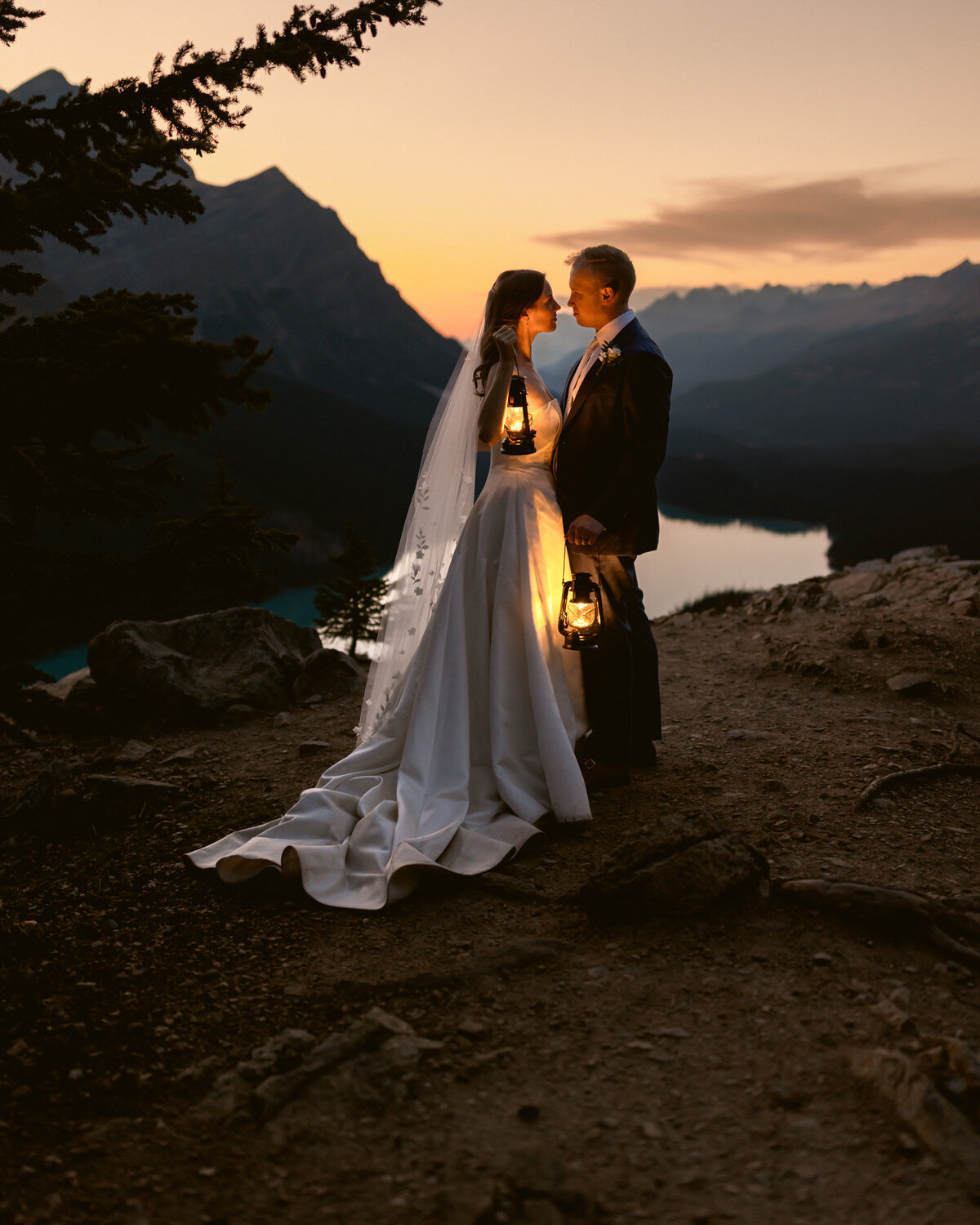 A breathtaking moment as a couple stands atop a mountain in Banff National Park by Moraine Lake with the bride’s dress flowing in the wind on a warm summer day. A dramatic photograph in the Canadian Rockies best elopement photographer captures the essence of adventure, love, and epic romance in the Canadian Rockies.