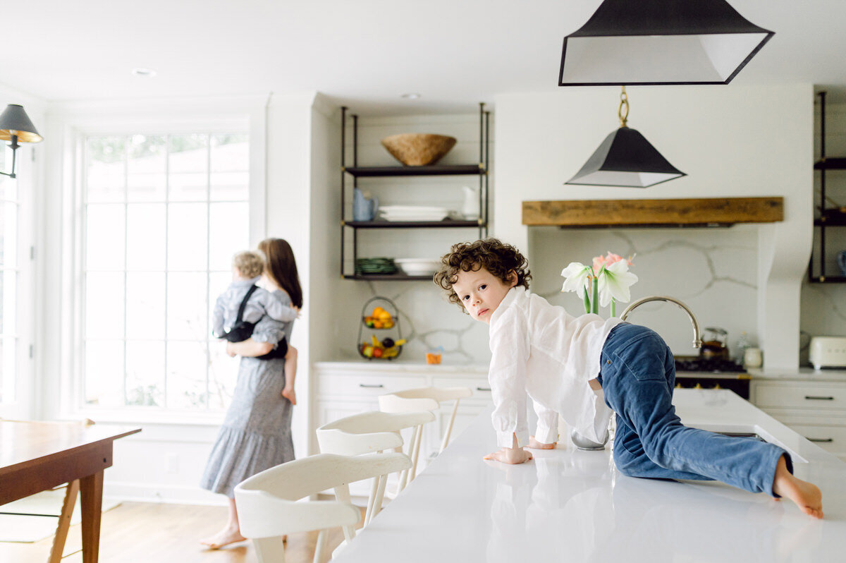 boy climbing on counter with mom walking by