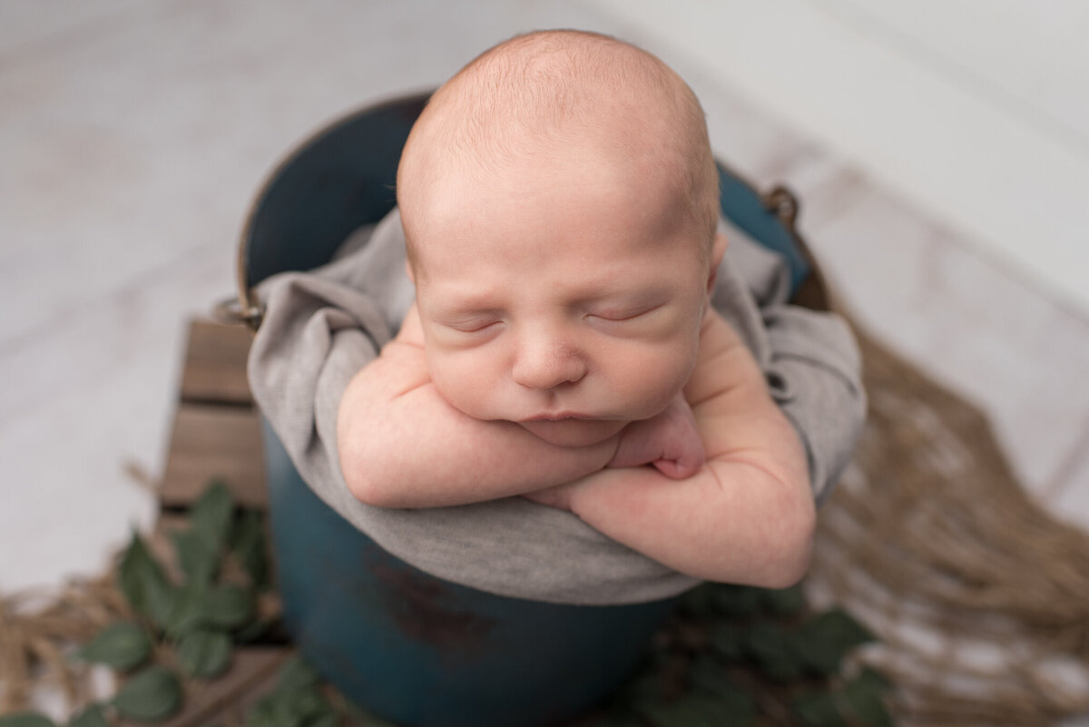 Baby boy with head on arms, in teal bucket