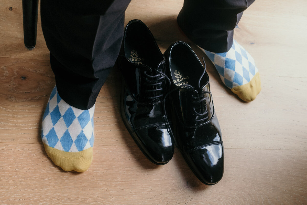 Nahaufnahme der Füße des Bräutigams in Socken mit weiß-blauem Rautenmuster mit schwarzem Lackschuhen mittig.