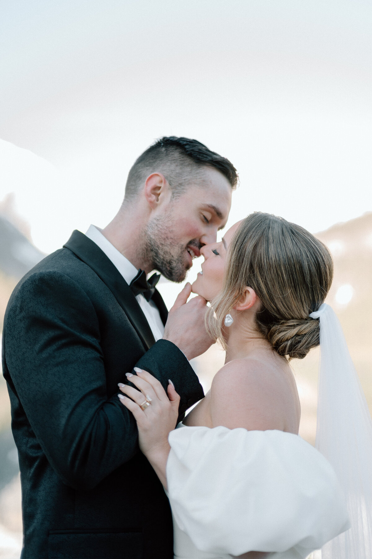 Groom gently touching bride’s chin in a romantic moment by the mountains