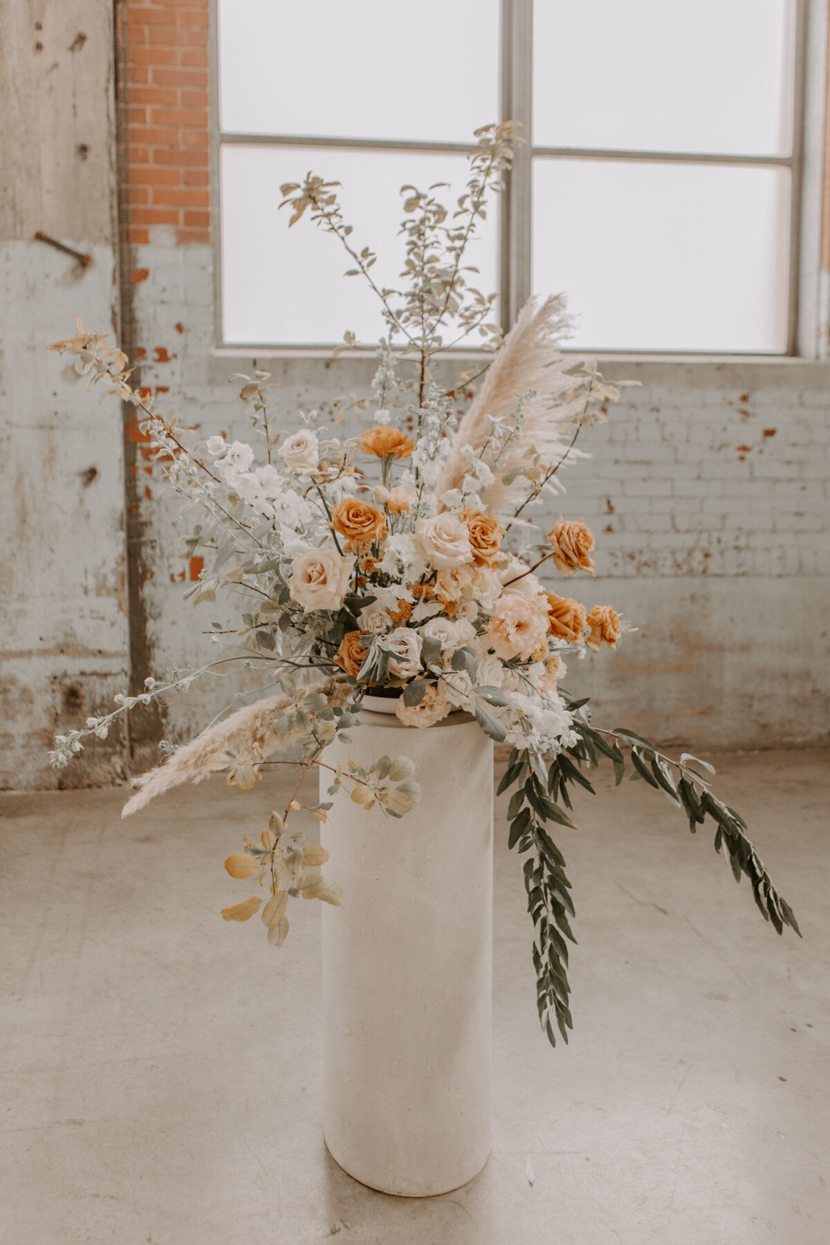 An orange and silver ceremony arrangement against a brick wall for a wedding at Fonderie Darling.
