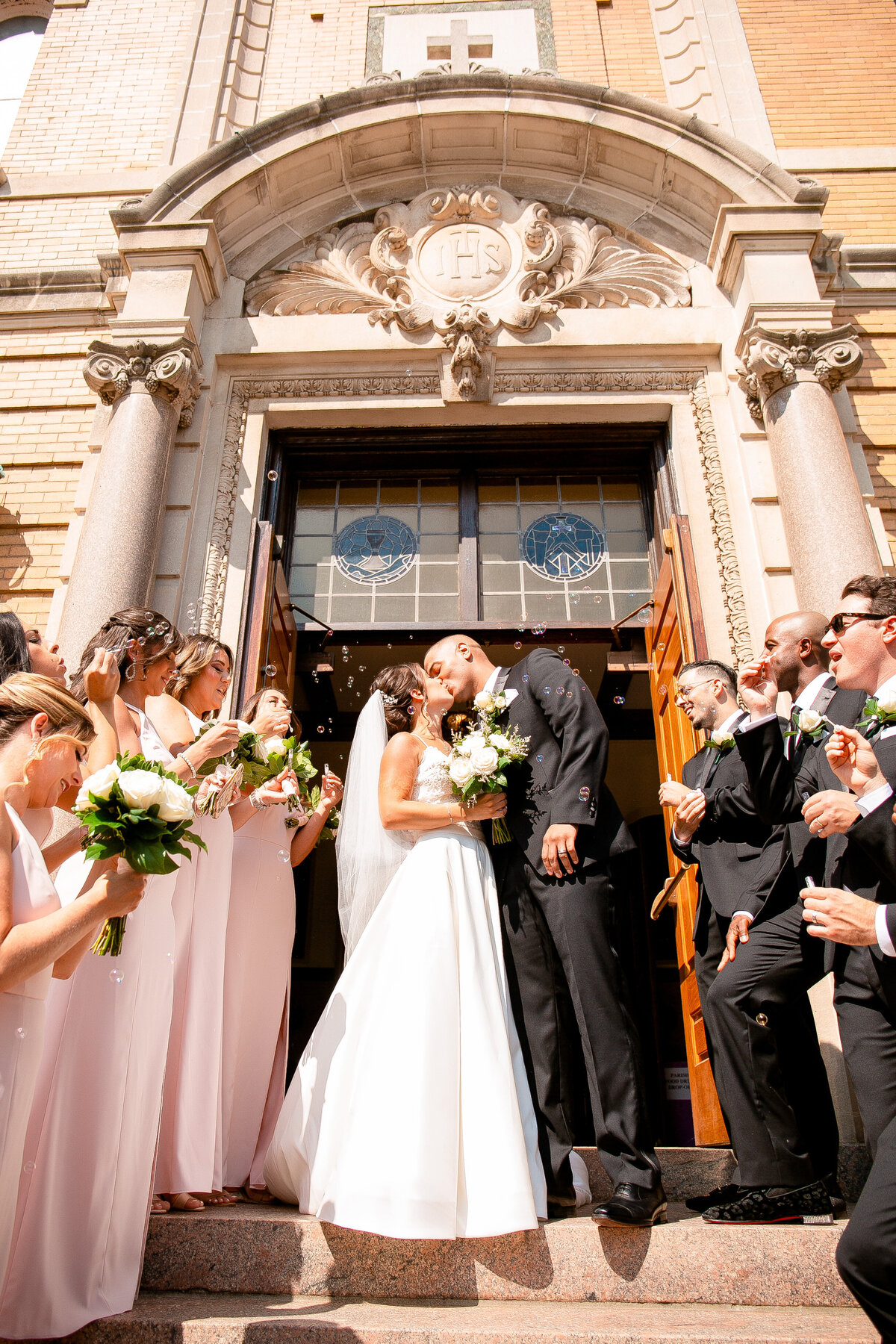 Newlyweds kiss as they leave the church and their wedding party blow bubbles.