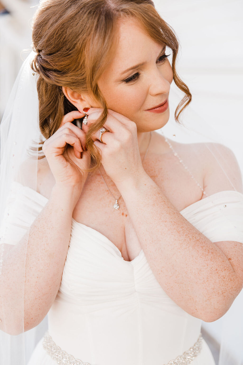 Elegant shot of the bride putting on her earrings, a moment that captures the intricate details and personal touches of her bridal attire