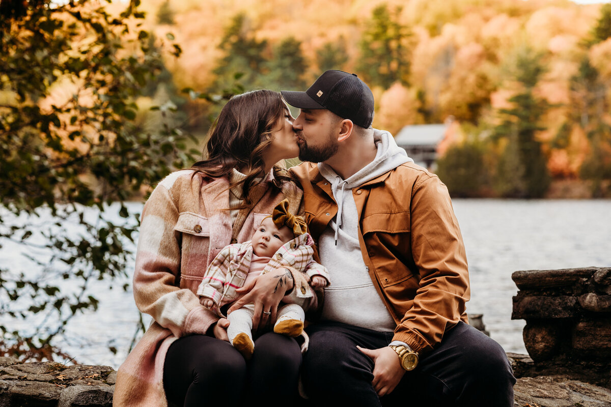 Couple kissing while holding their baby at Mackenzie King Estate in Gatineau Park