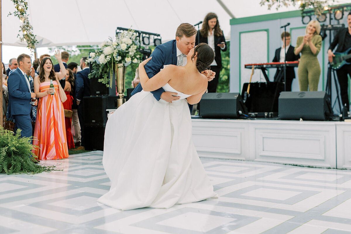 Groom dips bride during their first dance under a sailcloth tent at a spring mountain wedding in Cashiers, North Carolina.