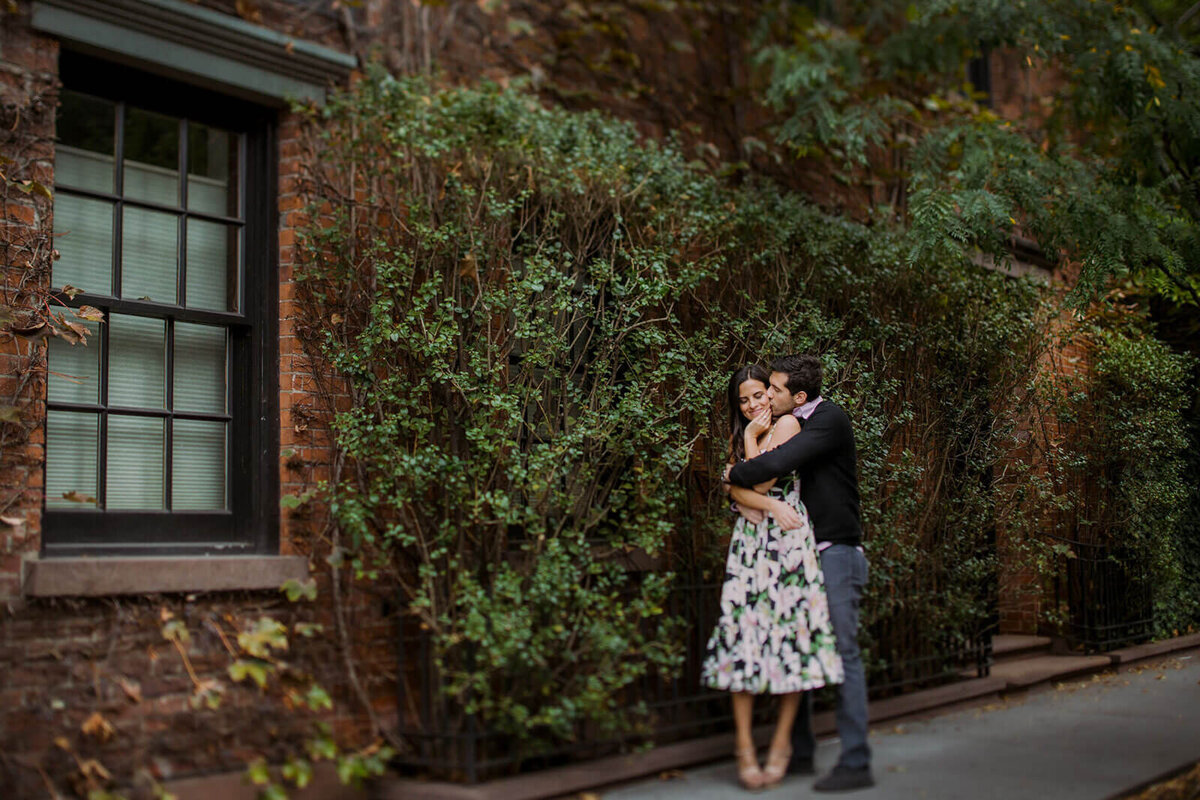 The man is kissing his fiancée in front of an ivy-covered building in West Village, Manhattan, NYC. Image by Jenny Fu Studio.