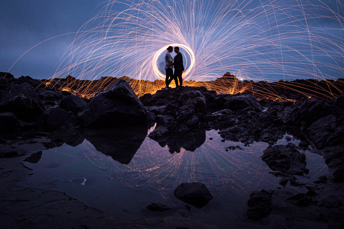 A dynamic and breathtaking photo of a couple on Agate Beach in Trinidad, CA, with golden sparks spinning behind them, creating a magical and cinematic effect against the coastal backdrop.